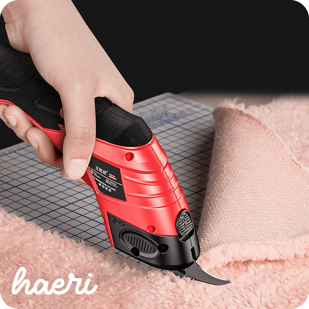 Electro fabric cutting tool by Haeri in use, cutting soft pink fabric on a grid surface.
