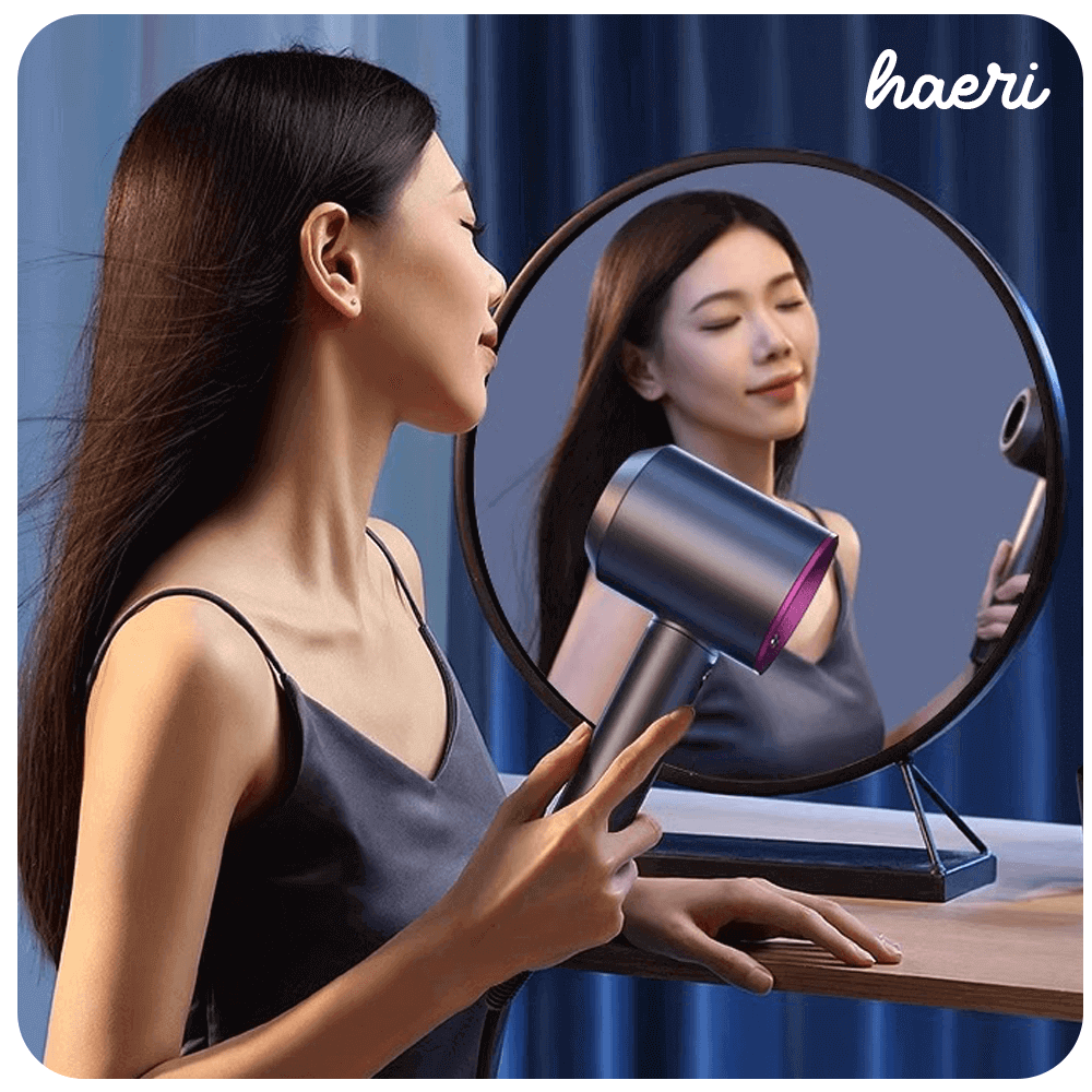 Person using a modern gray hair dryer with mirror reflection in a stylish setting.