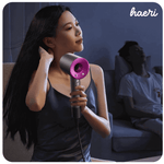 Woman using a modern hair dryer at night with sleeping person in the background.