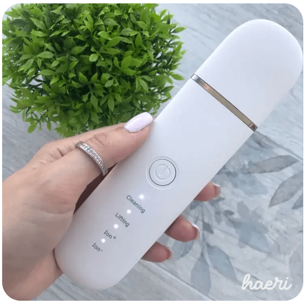 Ultrasonic skin scrubber in hand with buttons for cleaning, lifting, and ion functions on a stylish background.