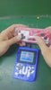 Hands holding a red joystick with a blue retro gaming console featuring the SUP logo and an LCD screen.